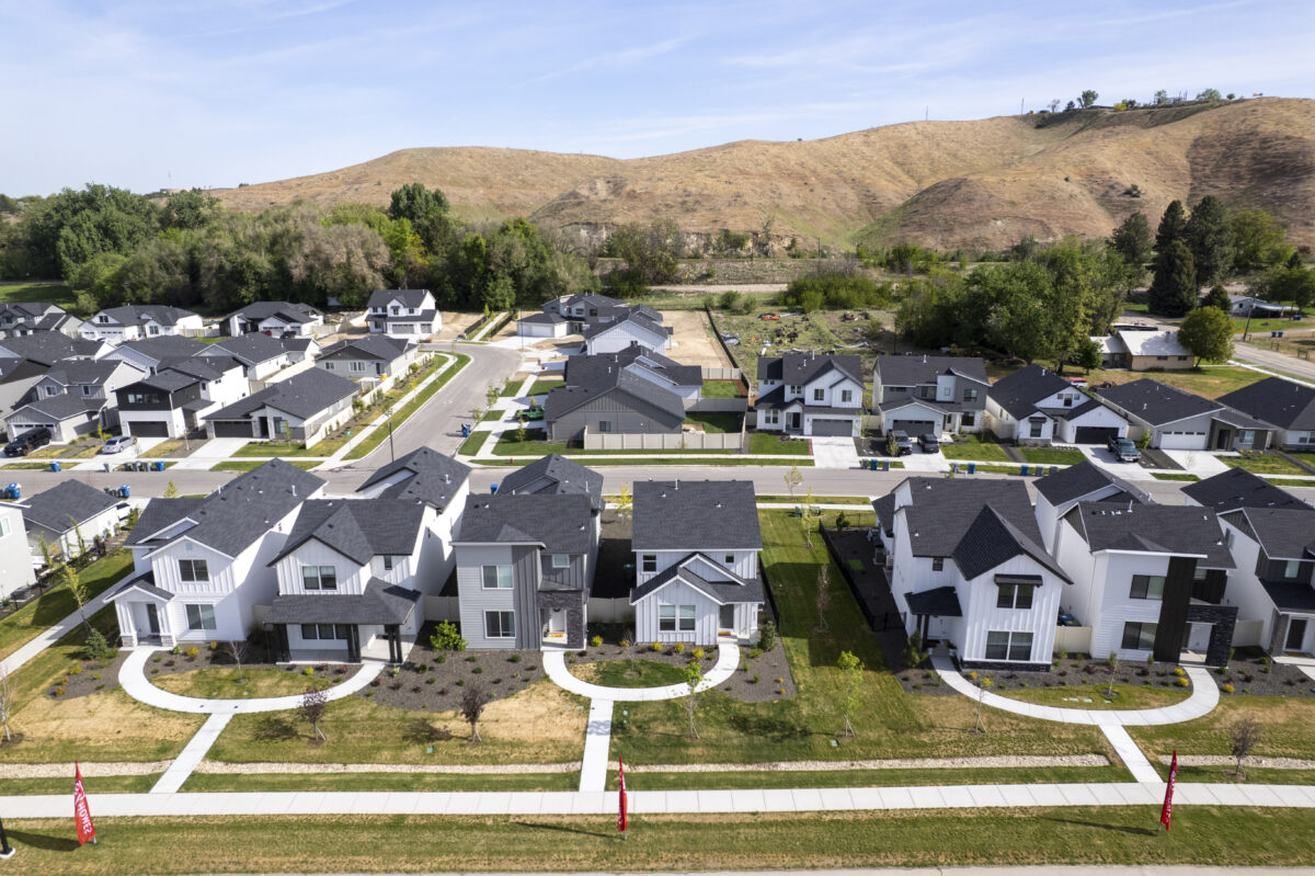 Ground-level aerial image highlighting a row of stylish new CBH Homes with front porches, large windows, and curved walkways leading to the sidewalk, against a hillside backdrop.