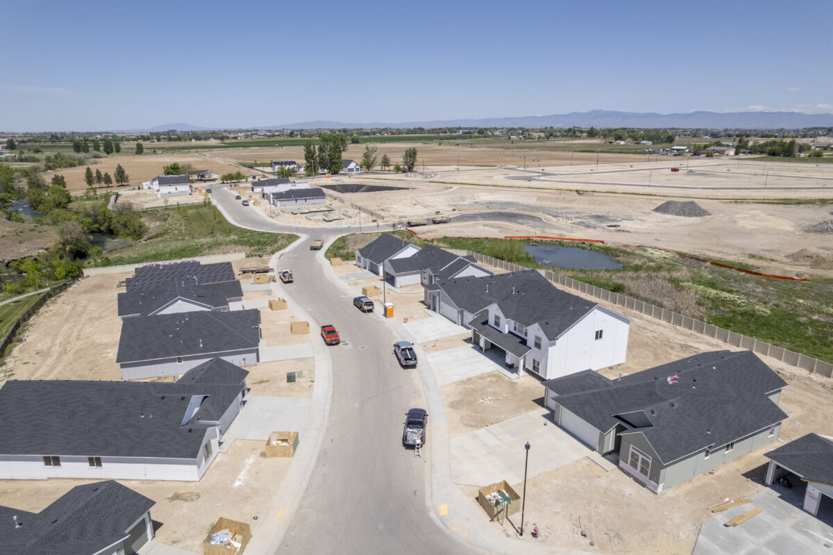Drone photo of a curved street under active development with trucks and materials onsite, surrounded by completed homes and farmland.
