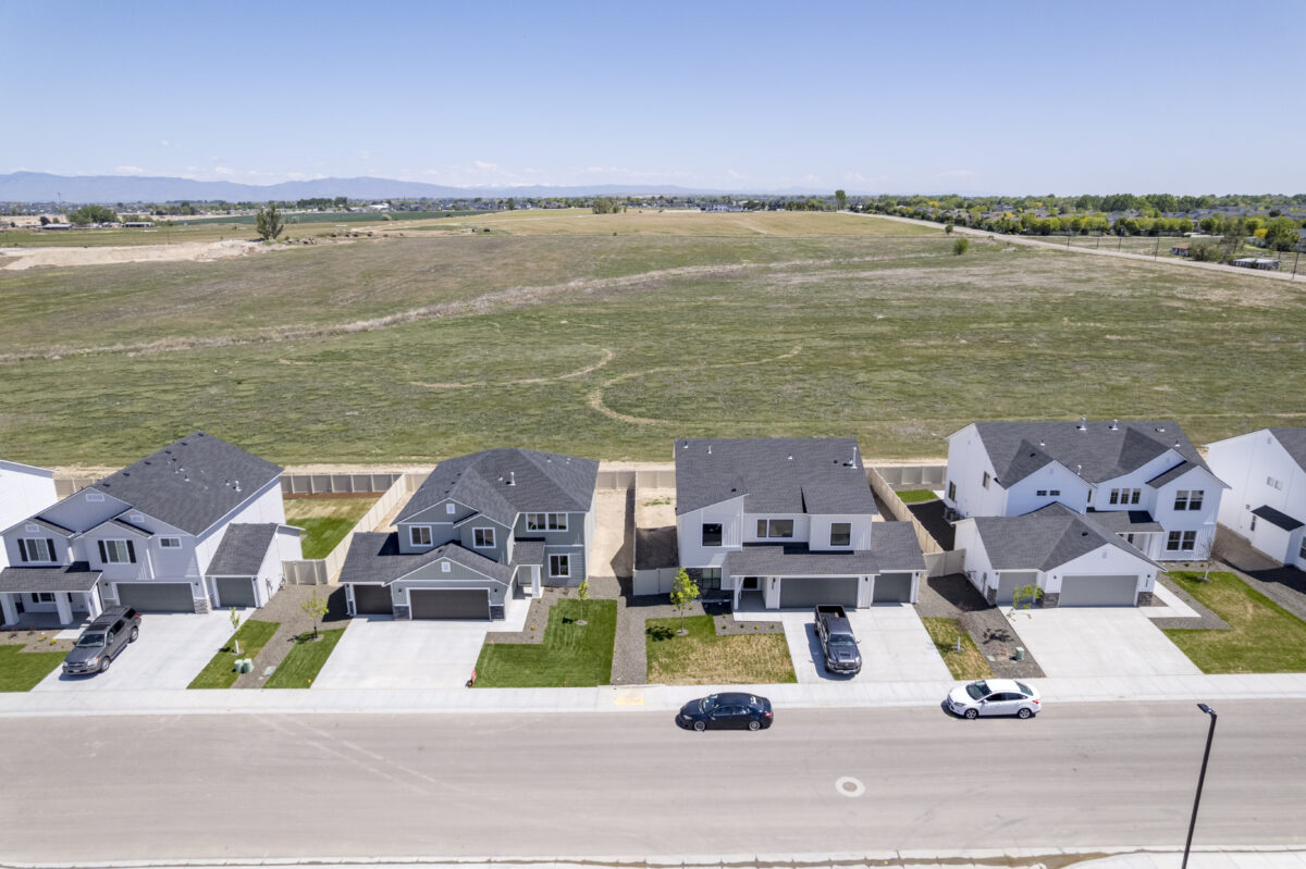 Drone shot capturing a full row of homes in front of an expansive undeveloped green field, illustrating the peaceful rural surroundings.