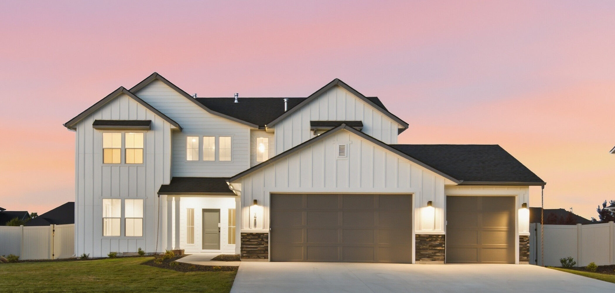 Two-story modern farmhouse-style home at sunset featuring white board-and-batten siding, a three-car garage, stone accents, and warm exterior lighting beneath a pink evening sky.