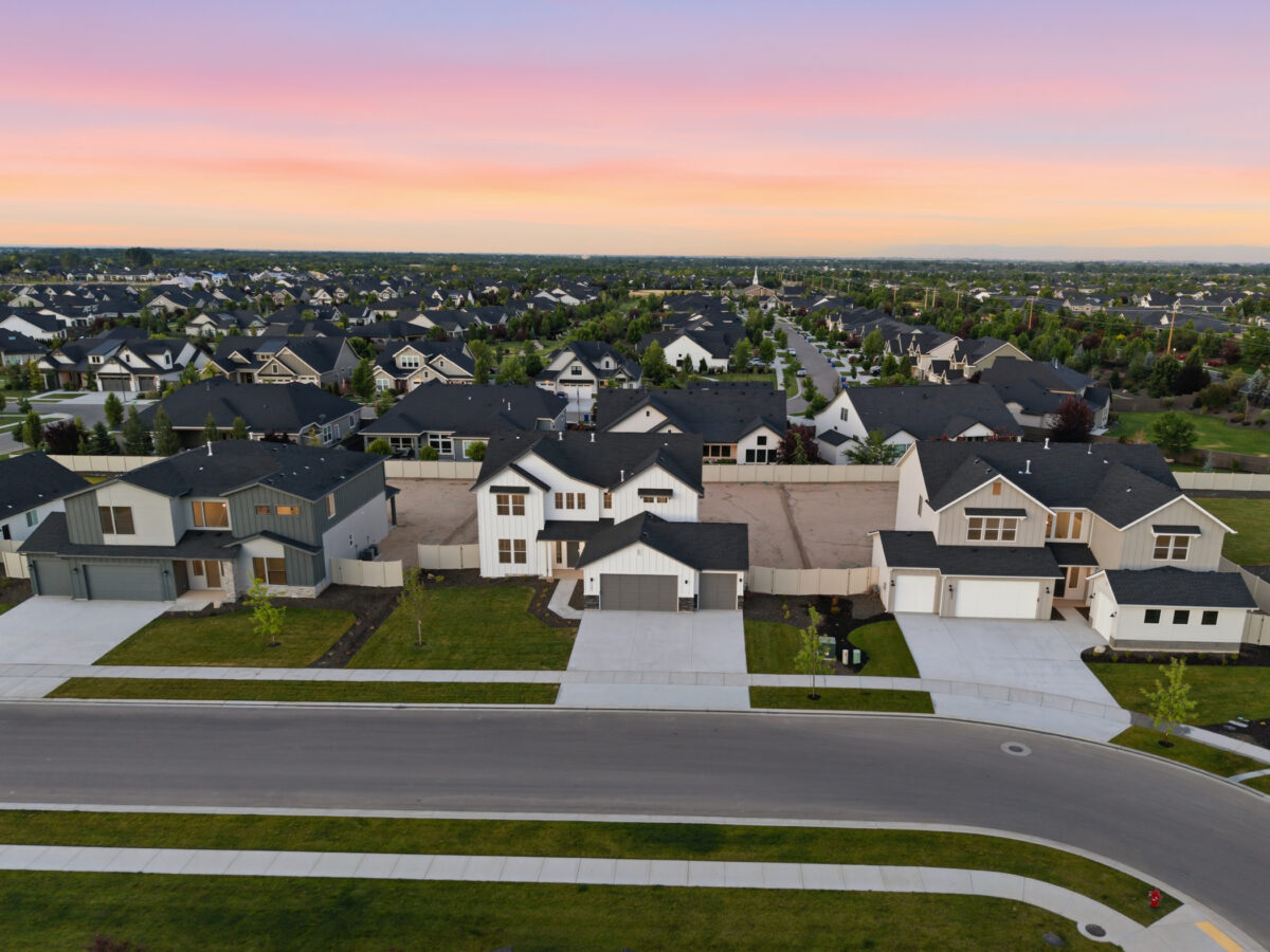 Aerial view of a new home community at sunset featuring modern homes, landscaped yards, curved streets, and a colorful pink and orange sky stretching across the horizon.