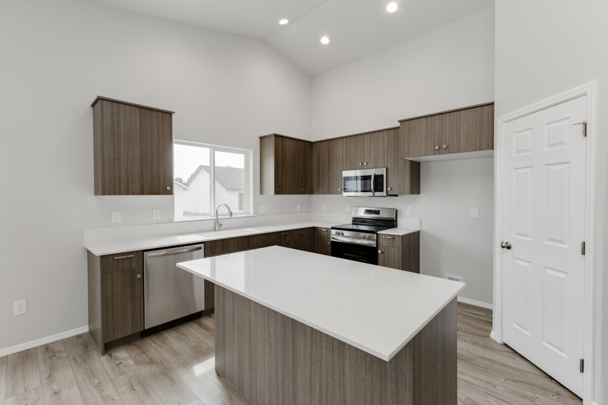 Elegant U-shaped kitchen with rich brown cabinets, stainless appliances, and bright white quartz countertops. The space includes a center island, large window above the sink, and soft recessed lighting. The mix of dark cabinetry and light finishes creates a stylish, modern contrast.