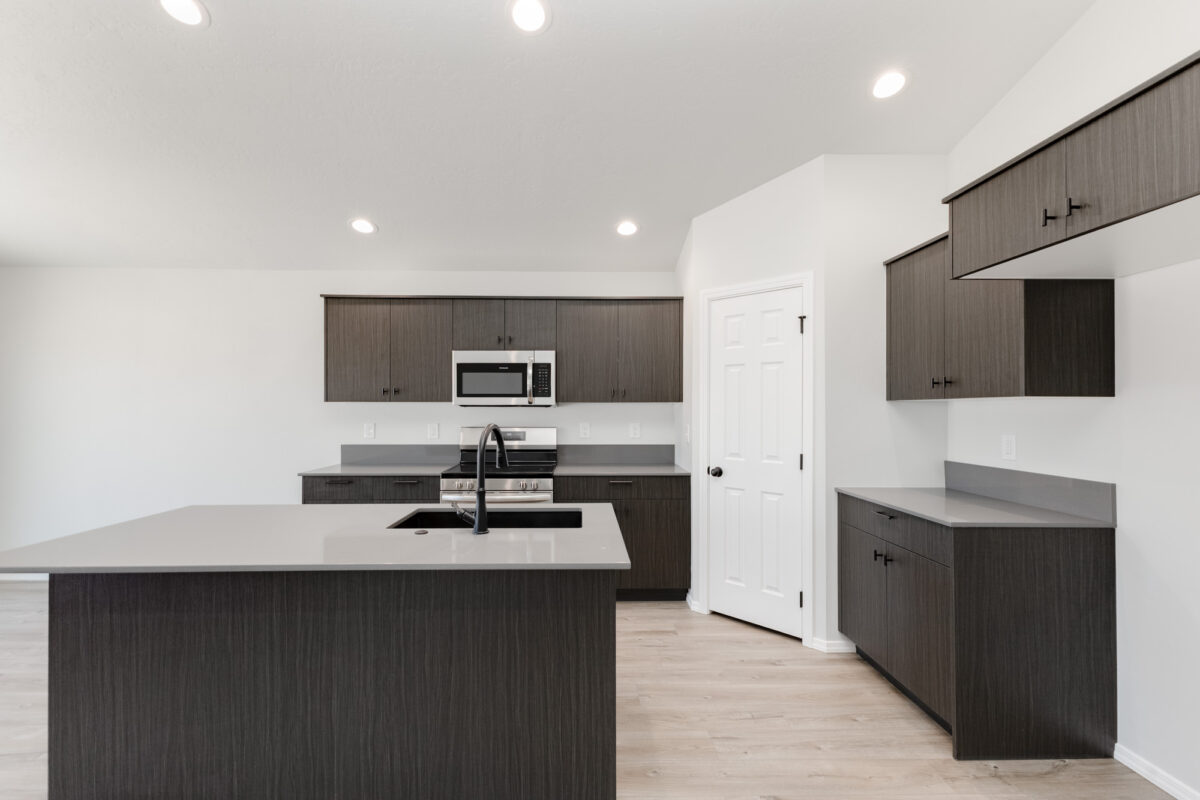 Bright kitchen featuring wood-grain cabinets and pure white quartz countertops. A central island provides additional workspace, while stainless steel appliances and large windows add functionality and natural light. Vaulted ceilings enhance the open and airy feel.