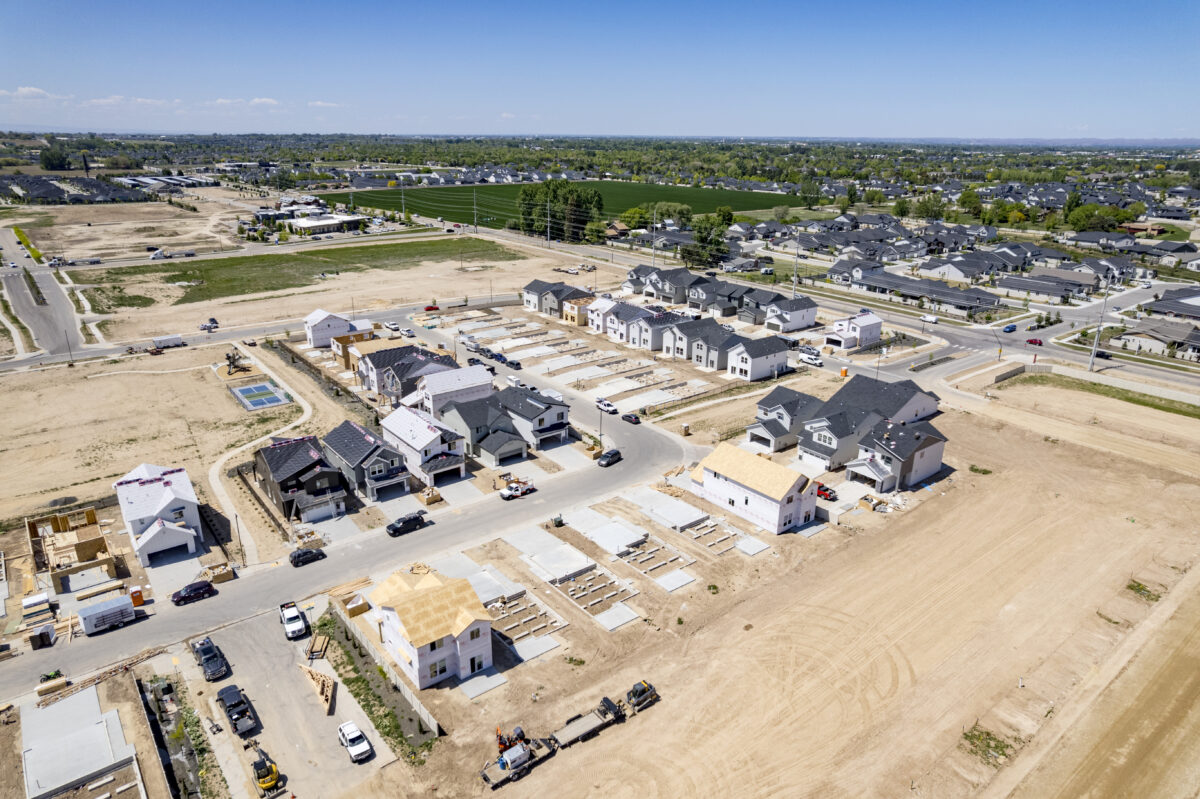 Drone shot of a CBH Homes development with newly poured foundations in rows, early-stage framing, and surrounding infrastructure taking shape in the distance.