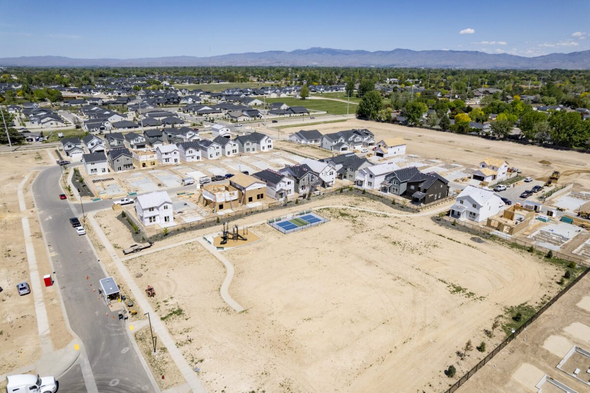 Expansive aerial view showing a future park area with a completed playground and pickleball court adjacent to rows of framed and finished homes under construction.