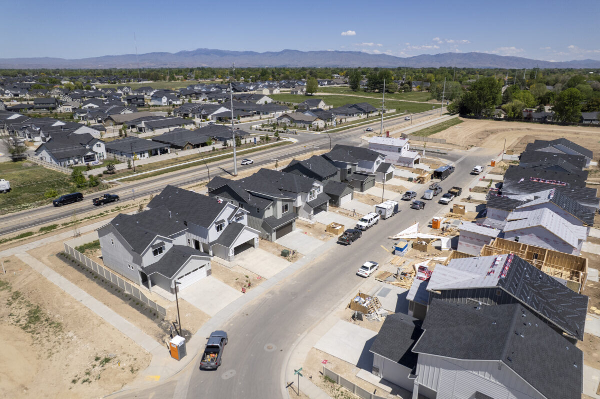 Aerial image of new homes under construction along a residential road, adjacent to a major street, with framing underway and building materials scattered across lots.