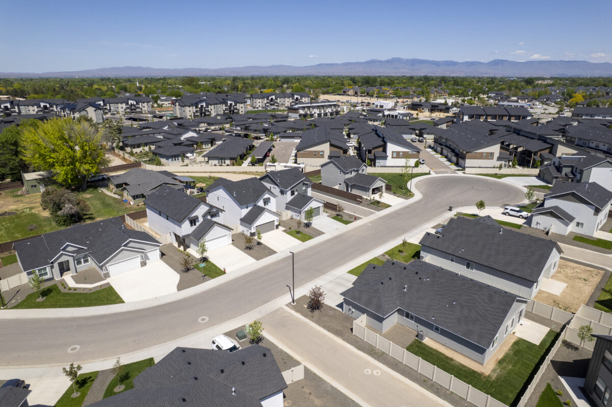 Expansive community overview showing the full Dutton Place development, apartment communities in the distance, and green trees under a clear blue sky with mountain views.