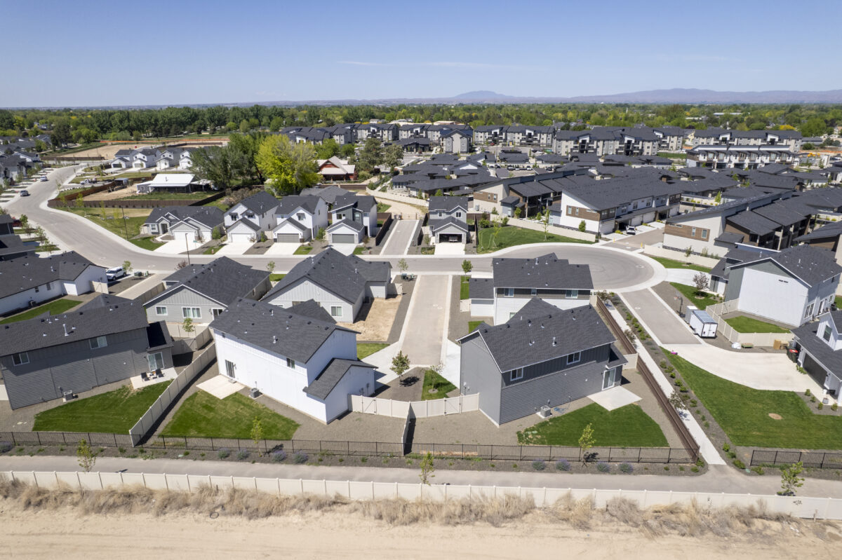 Drone perspective of fenced backyards, green lawns, and a walking path along a property line, with modern gray and white homes built closely together in a quiet cul-de-sac.