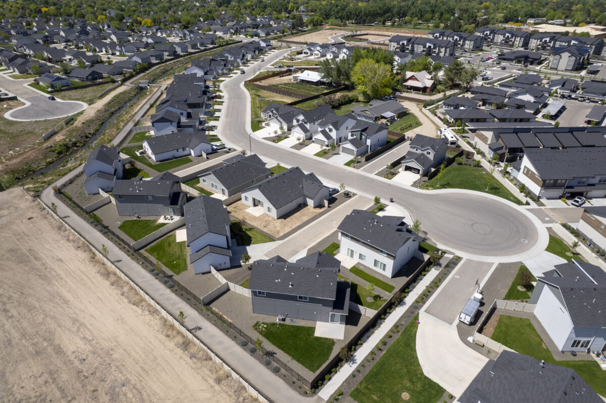 Broad aerial view from behind the homes, showing private fenced yards, back patios, and a pedestrian walking path dividing the new community from undeveloped land.