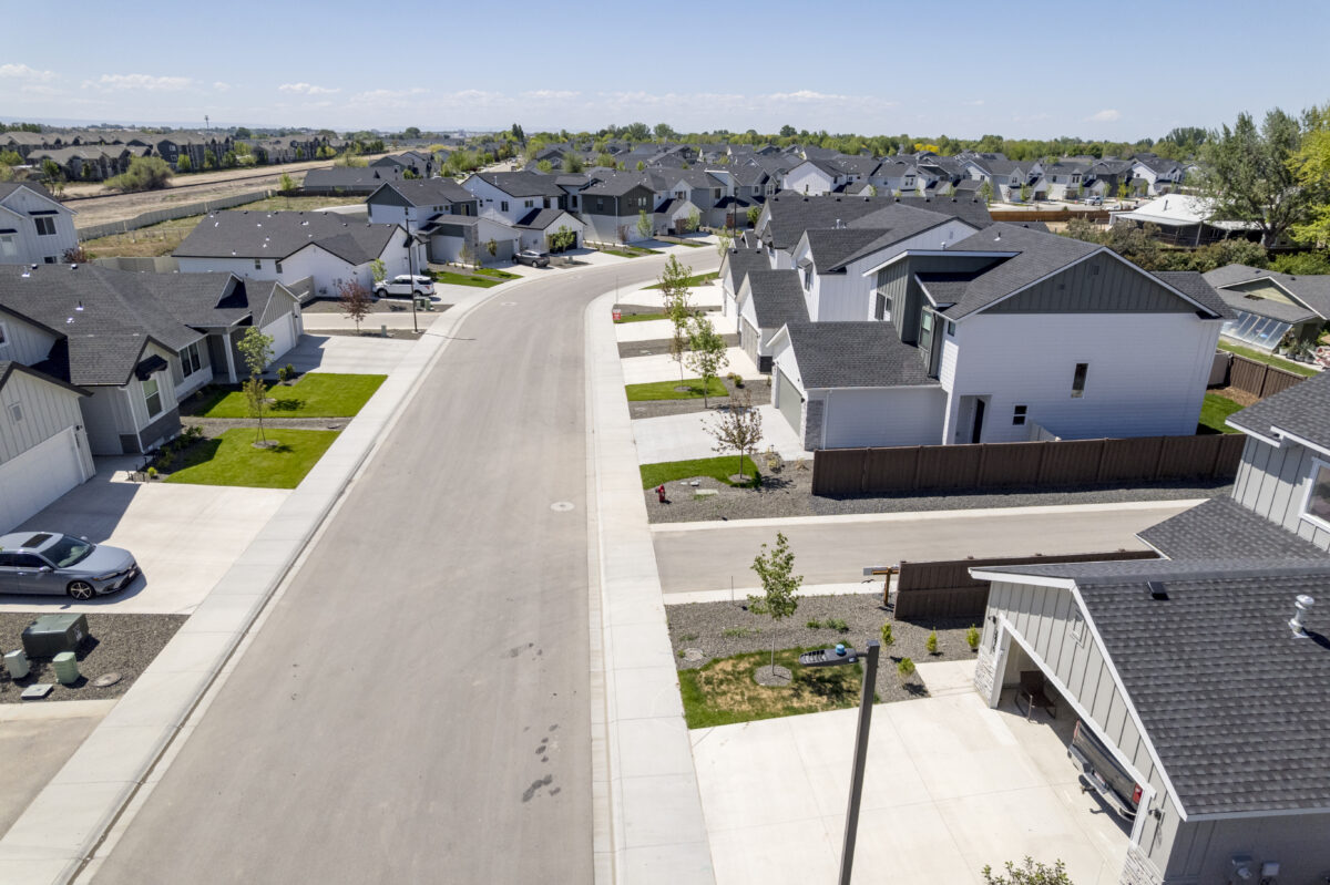 Drone shot of a smooth winding street lined with CBH homes, all with completed driveways, lawns, and freshly planted trees in a neatly planned residential setting.