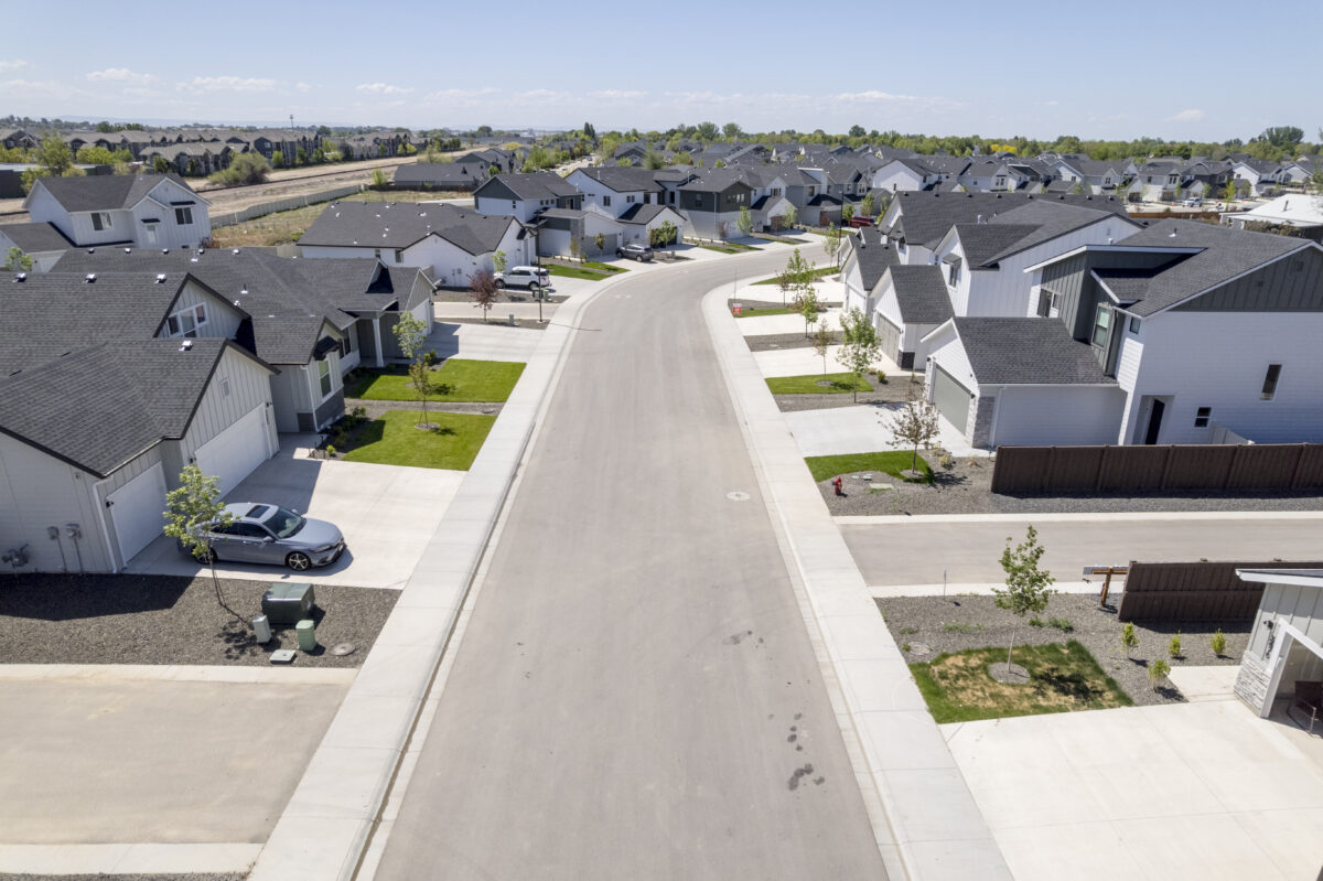 Overhead image of a peaceful street lined with new CBH homes in various styles, flanked by lawns, sidewalks, and a backdrop of established residential rooftops.