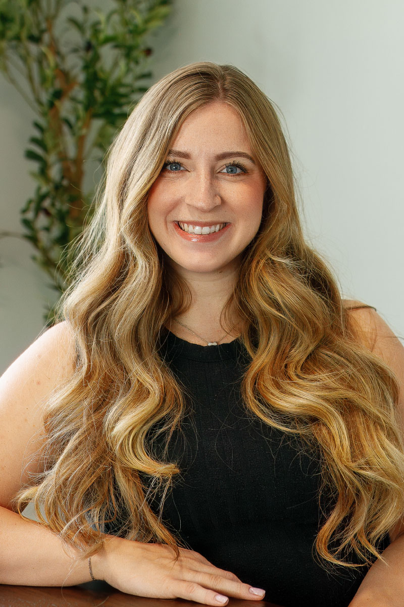 Smiling woman with long wavy blonde hair in a black top, professional headshot for CBH Homes website.