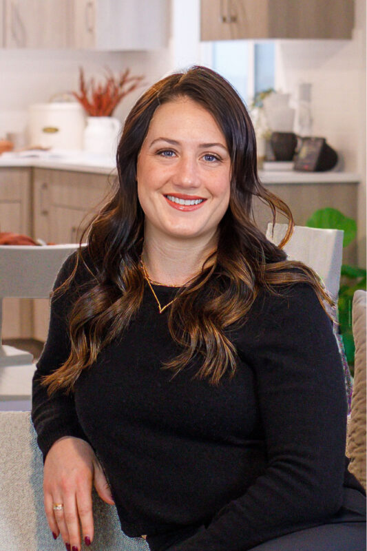 Professional headshot of Alexis, an agent at CBH Homes, smiling with long brunette hair in a warm, inviting kitchen setting