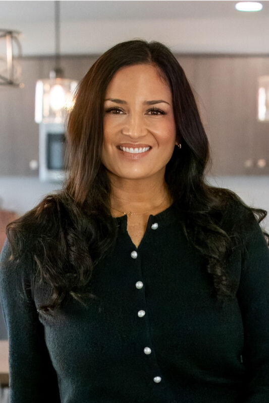 Professional headshot of a smiling woman with long dark hair, wearing a black button-up sweater.