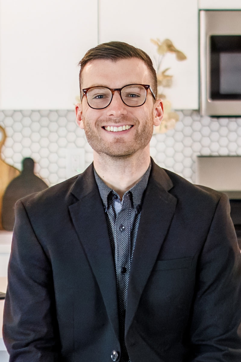 Professional headshot of Nick Hafner, an agent at CBH Homes, smiling with glasses in a modern, bright kitchen setting
