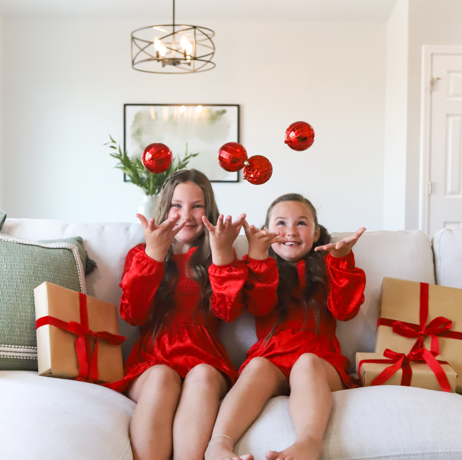 Two girls tossing ornaments in the air on a festive couch