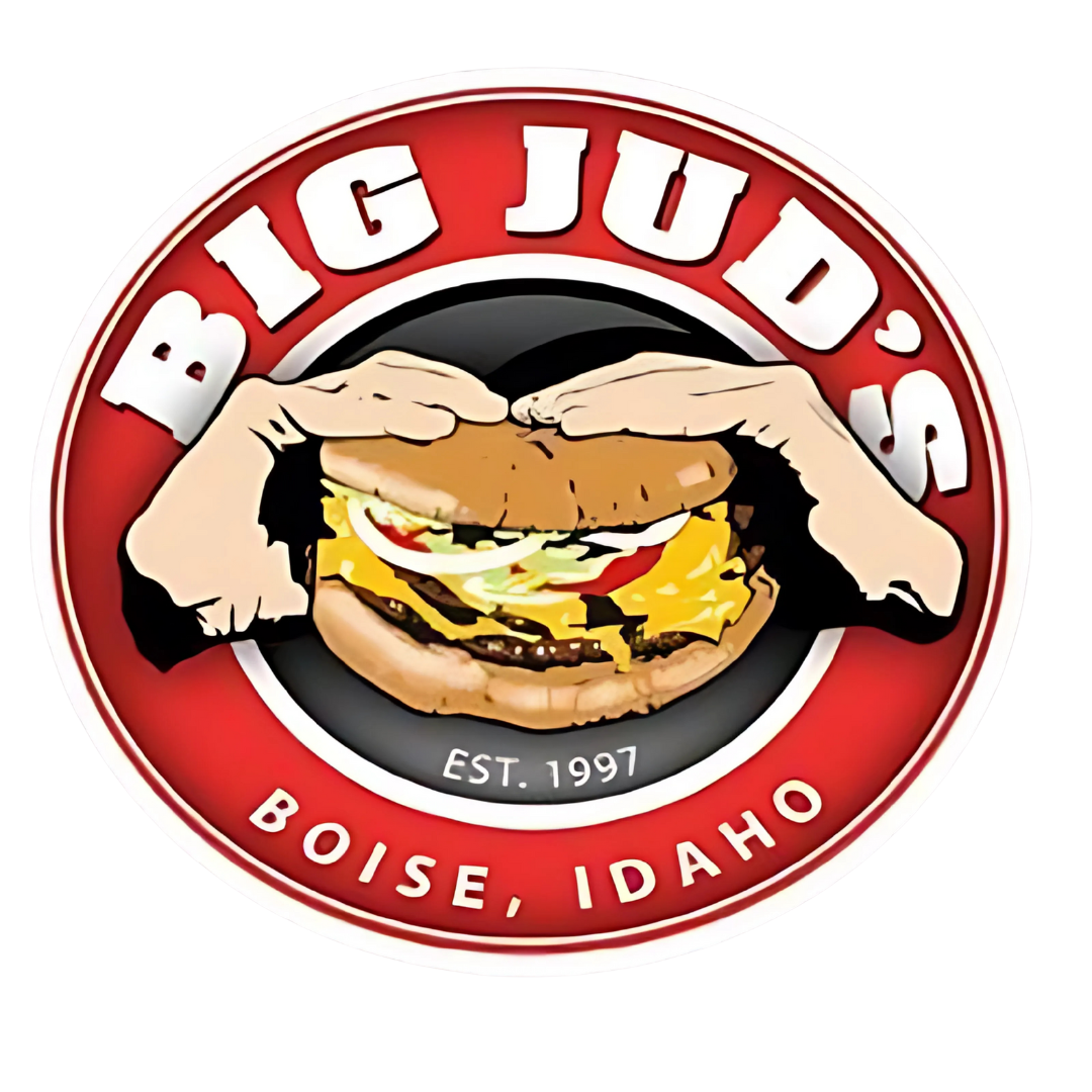 Logo for Big Jud's, a burger restaurant established in 1997 in Boise, Idaho. The logo features two cartoon hands holding a large cheeseburger with visible layers of lettuce, tomato, onions, and melted cheese. The text 'BIG JUD'S' curves around the top in bold white letters on a red background, and 'BOISE, IDAHO' is written at the bottom.