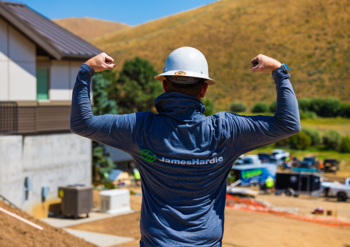 Construction worker wearing a James Hardie shirt and hard hat flexing on a job site in Idaho, showcasing strength and siding partnership with CBH Homes.