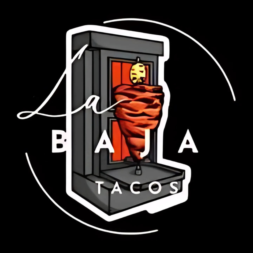Logo for "La Baja Tacos" featuring a vertical trompo (meat rotisserie) inside a stylized taco stand or vertical spit oven. The word "Baja" is displayed in bold white capital letters across the middle, with the cursive word "La" overlaid at the top and "TACOS" at the bottom. The logo is set against a black background with a circular white line partially enclosing the design.