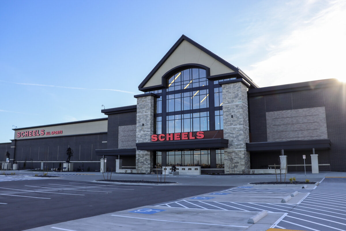Exterior of SCHEELS store in Meridian, Idaho, featuring stone and glass facade with red signage under a clear blue sky.