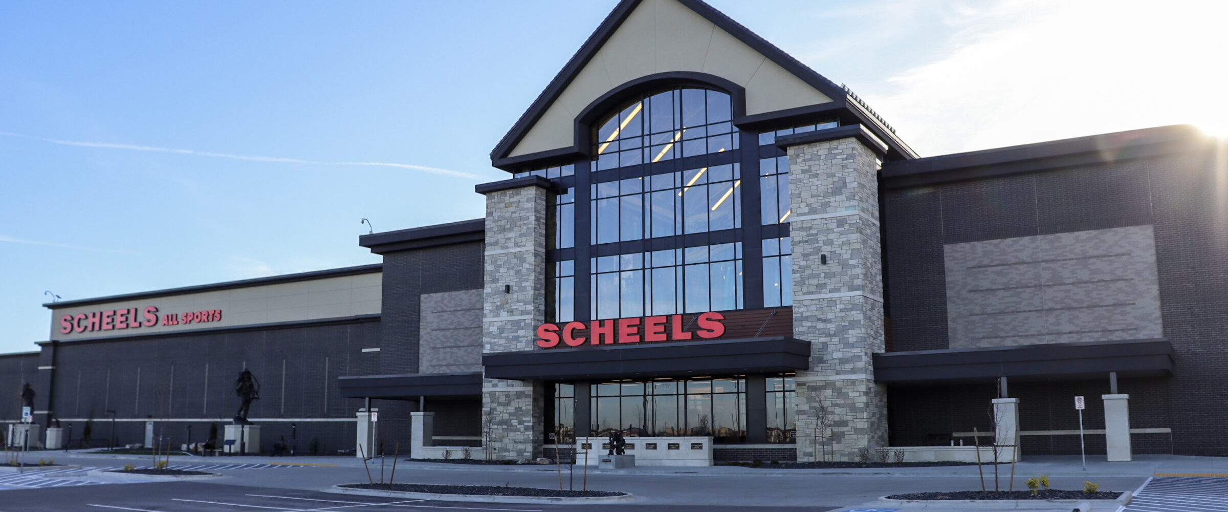 Exterior of SCHEELS store in Meridian, Idaho, featuring stone and glass facade with red signage under a clear blue sky.