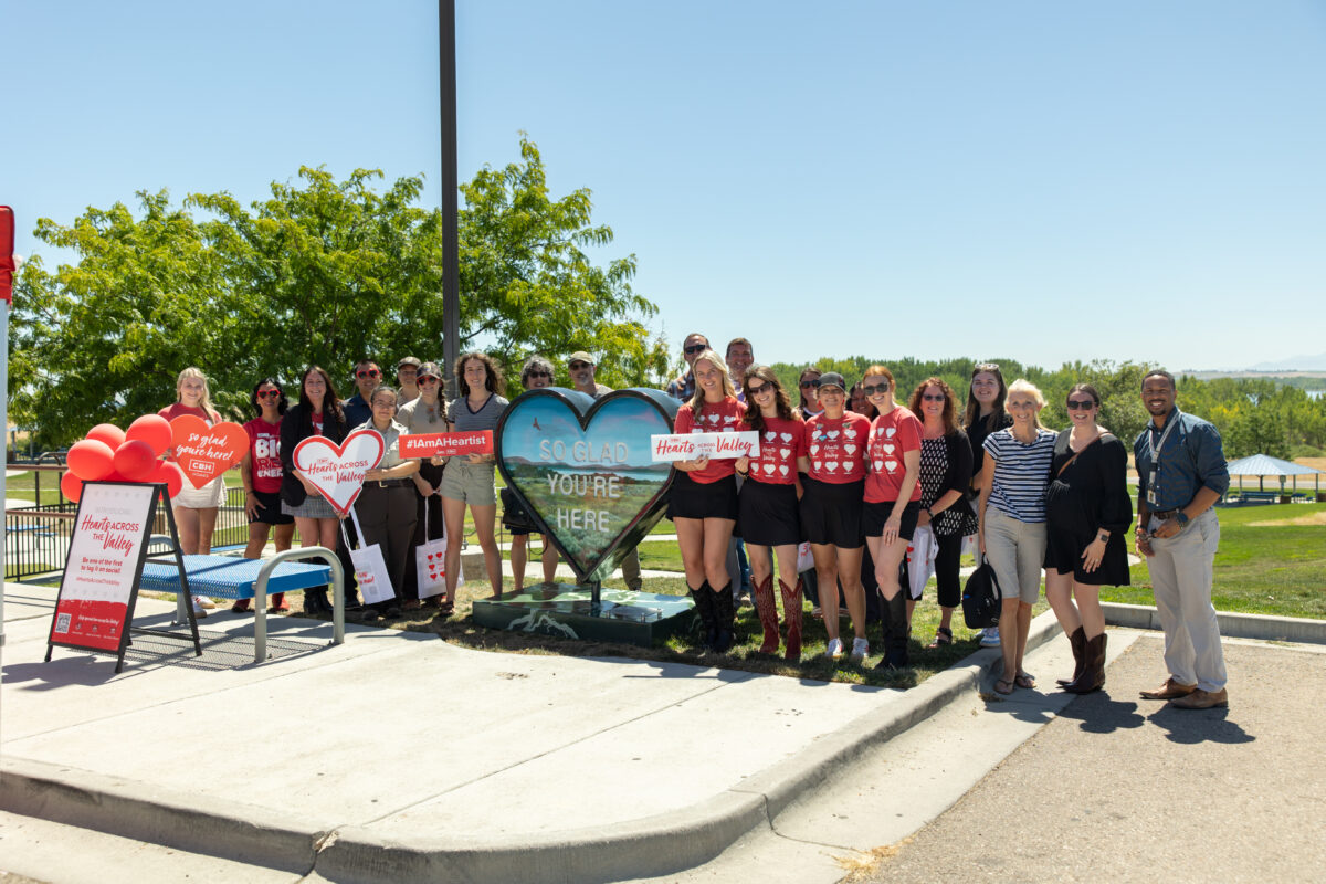 Group photo at the Hearts Across the Valley art event in Caldwell, Idaho, featuring community members and CBH Homes team around the “So Glad You’re Here” heart installation at Mallard Park.