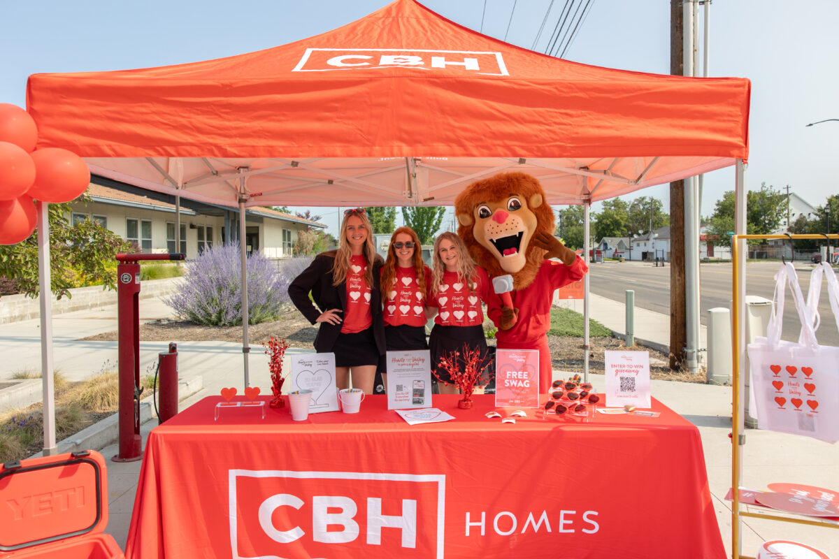 CBH Homes team and mascot at Hearts Across the Valley community event booth with giveaway items and branded red canopy