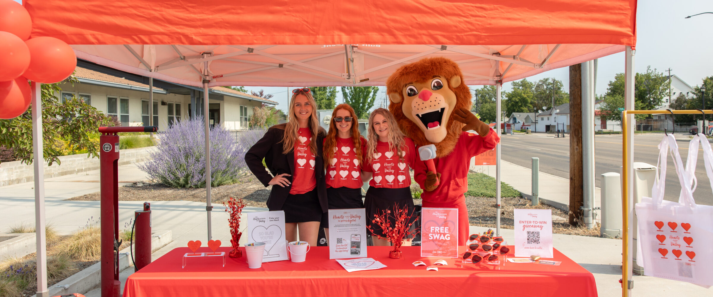 CBH Homes team and mascot at Hearts Across the Valley community event booth with giveaway items and branded red canopy