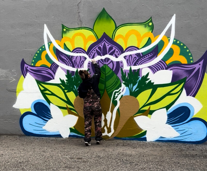 artist brianna gilbert with painted mural on wall