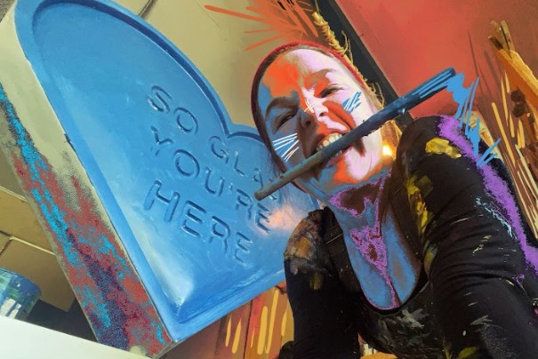 lady with a paintbrush in her mouth and blue painted heart in background