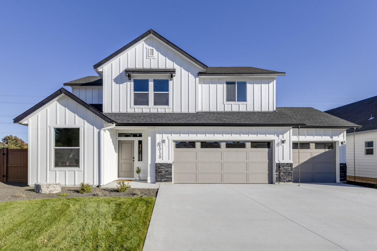 Modern new construction two-story home with white board-and-batten siding, black roof, large driveway, and attached three-car garage.