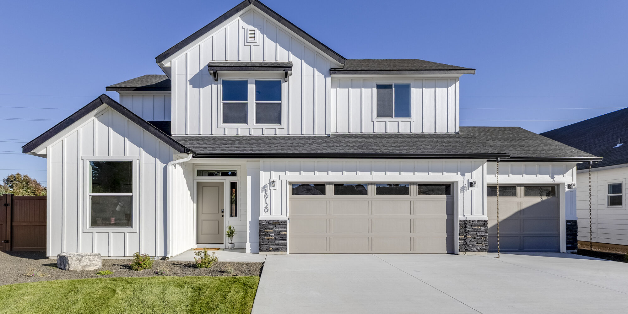 Modern new construction two-story home with white board-and-batten siding, black roof, large driveway, and attached three-car garage.