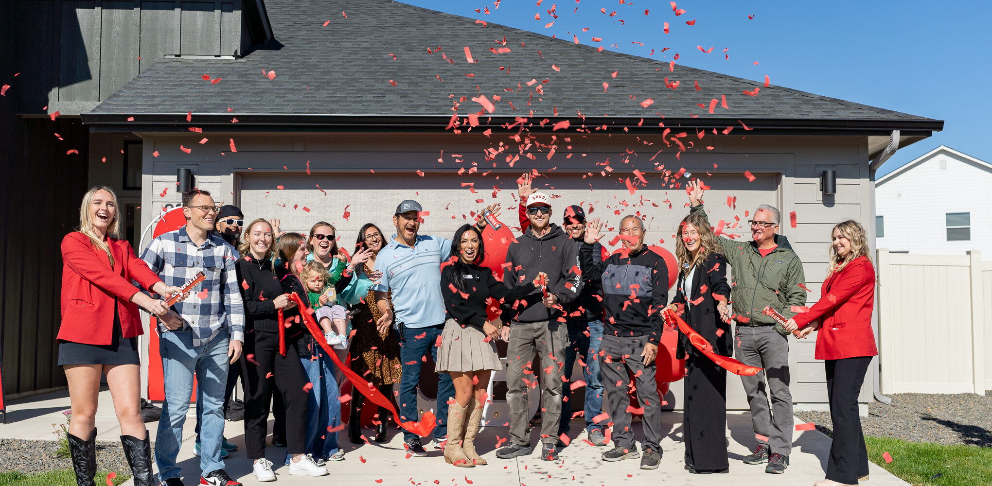CBH Homes team and homeowners celebrating a ribbon-cutting ceremony at the grand opening of a new community with confetti in front of a new home.