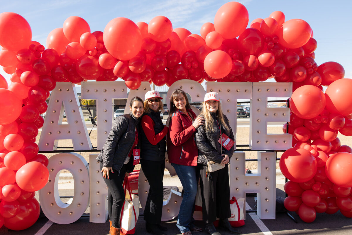 Four women pose smiling in front of a red balloon arch and large marquee letters that spell “A TASTE OF CBH”
