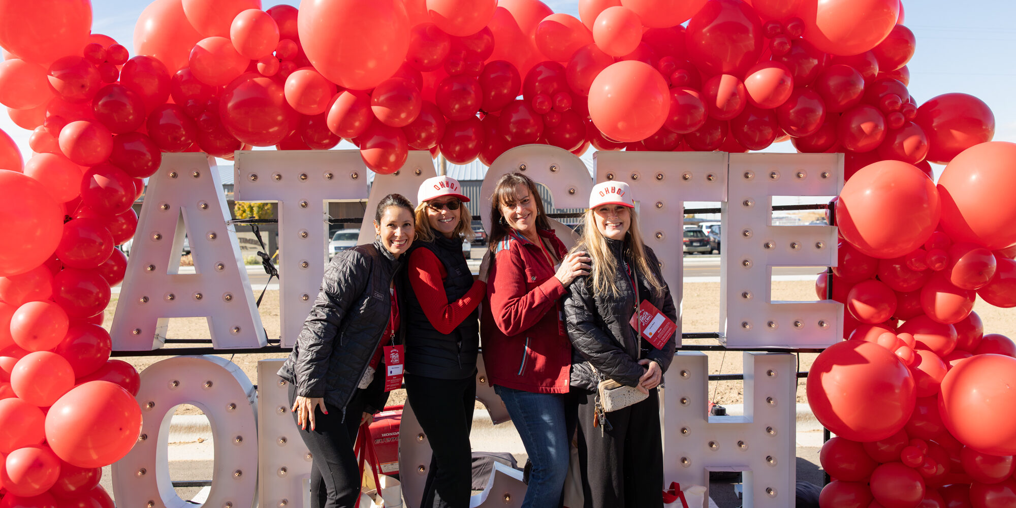 Four women pose smiling in front of a red balloon arch and large marquee letters that spell “A TASTE OF CBH”