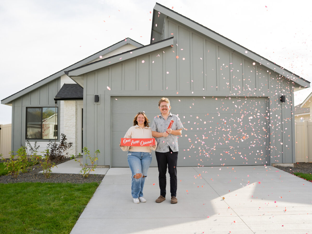 Smiling new homeowners celebrate in front of a modern Idaho home as red confetti falls, representing a thoughtfully designed 2026 home built to grow with changing lifestyles.