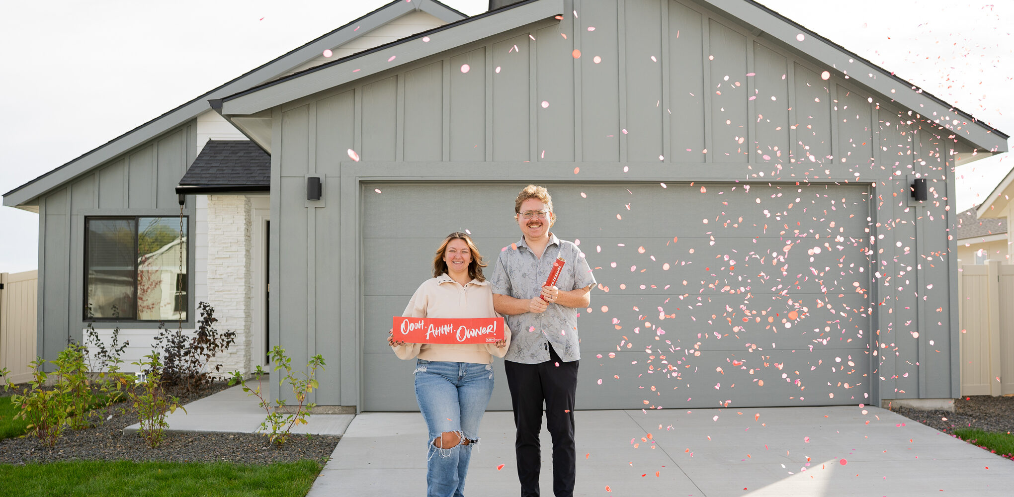 Smiling new homeowners celebrate in front of a modern Idaho home as red confetti falls, representing a thoughtfully designed 2026 home built to grow with changing lifestyles.