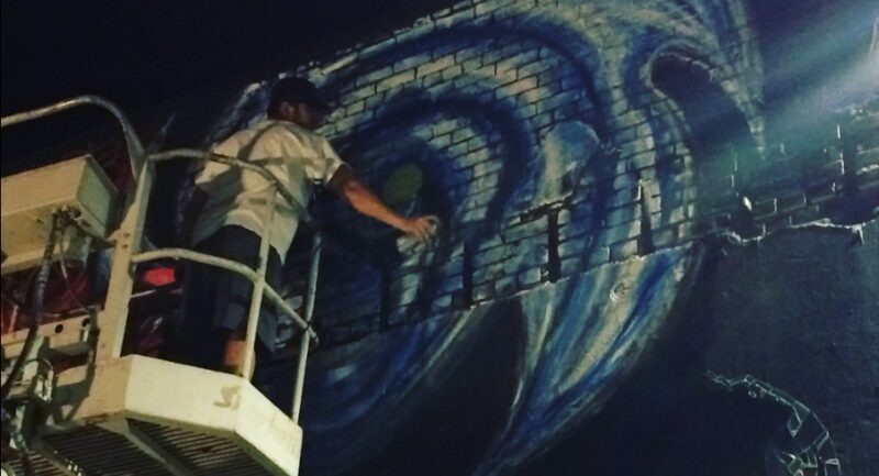 Artist Erik Diehl painting a blue and white mural on a brick wall
