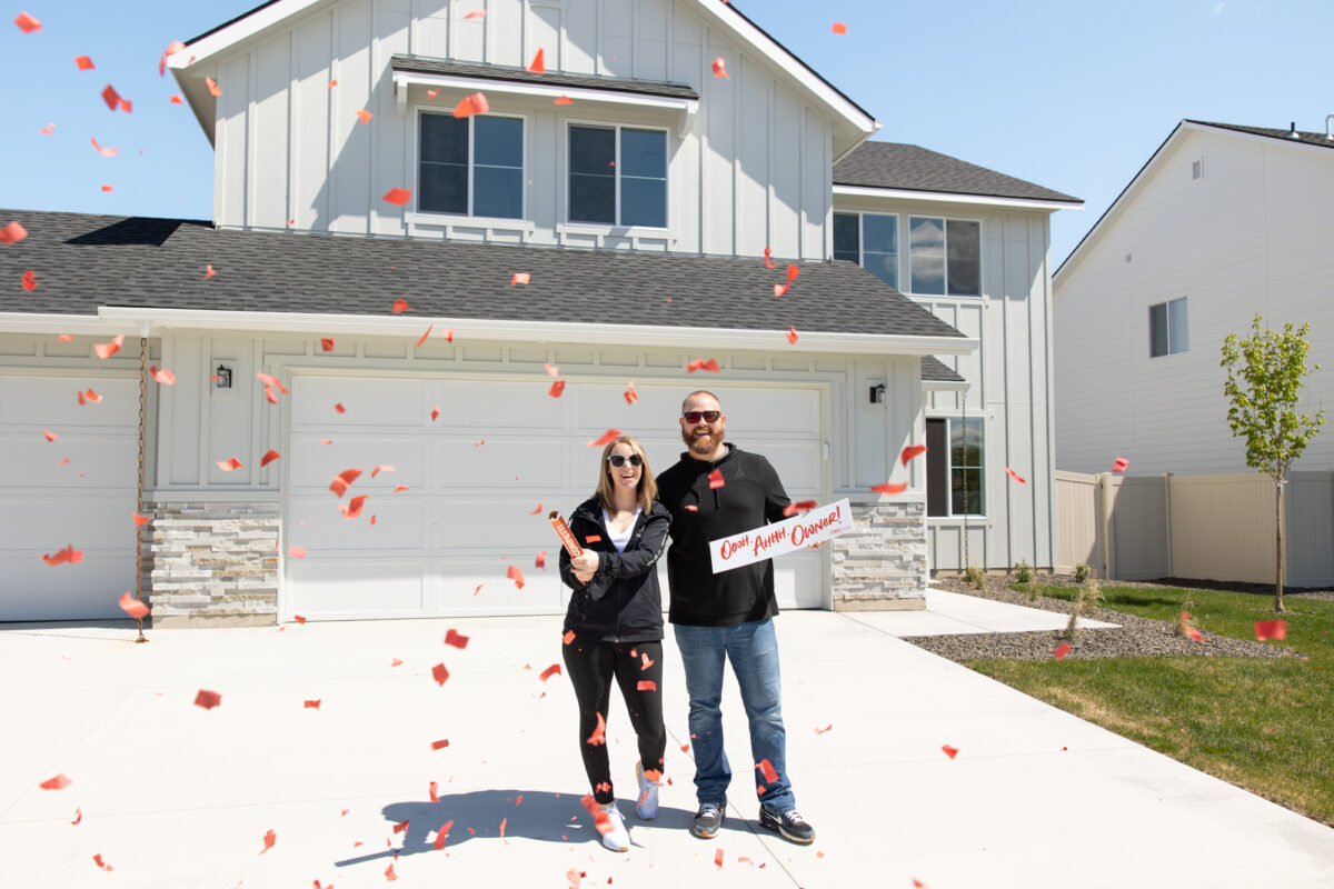 Happy couple celebrating in front of their new CBH home with red confetti, showcasing the excitement and joy of new homeownership in Idaho.