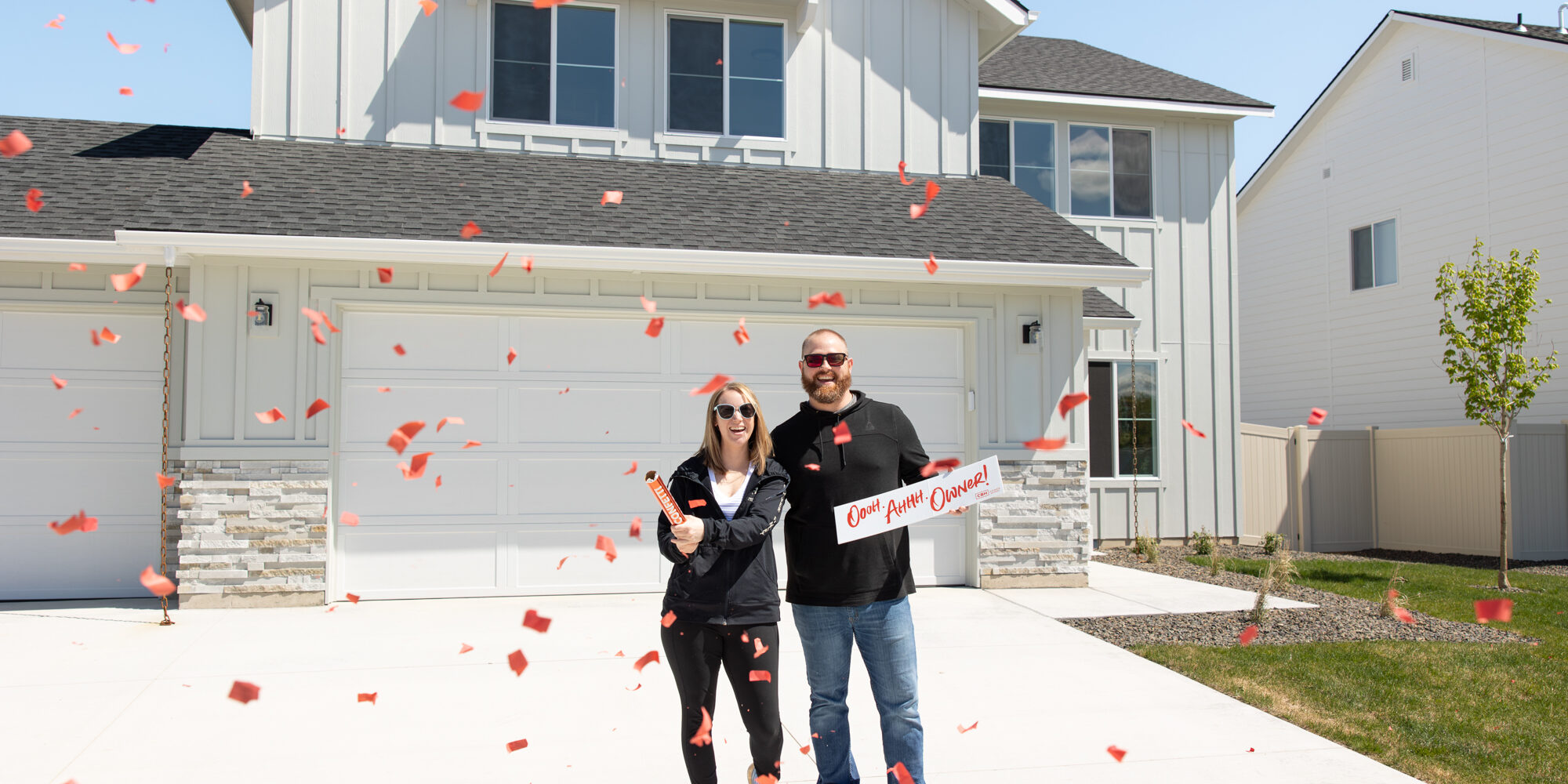 Happy couple celebrating in front of their new CBH home with red confetti, showcasing the excitement and joy of new homeownership in Idaho.